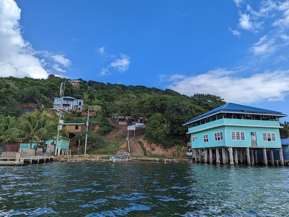 Blue wooden stilt house with a teal roof over the water in Oak Ridge, Roatán